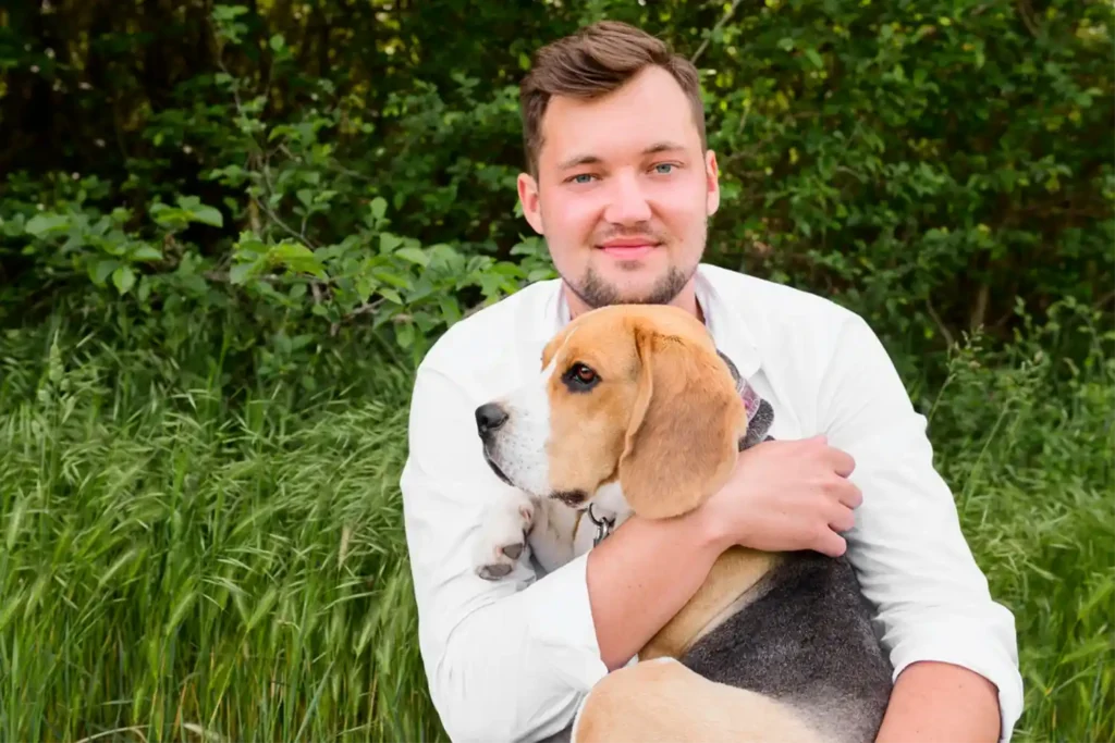 Man sitting on lawn cuddling his beagle, both looking content and relaxed, showcasing the breed's affectionate nature with family members